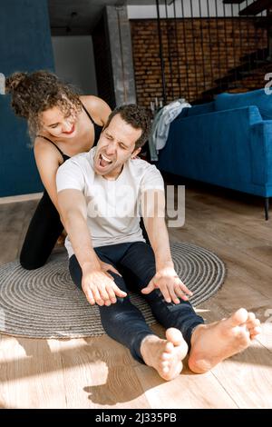 Fit jungen Mann macht Sport zu Hause mit Laptop auf dem Boden liegend mit Freundin Unterstützung helfenden Freund, sportliche weibliche Ausbildung Mann bei Stockfoto