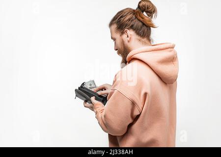 Mann, der auf grauem Hintergrund Papiergeld in der Brieftasche hält. Hand ziehen 100-Dollar-Banknoten aus der Brieftasche. Mann hat Bargeld. Das Konzept von Geld, Gehalt, Stockfoto