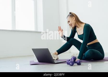 Online-Übungssitzung Marathon, Ferntraining. Glückliche Millennial-Frau, die auf dem Boden sitzt und mit Trainer spricht, Videoclip mit Lehrer hat, Stockfoto