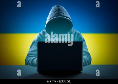 Gesichtsloser anonymer Computerhacker mit Kapuze auf ukrainischem Hintergrund. Internetkriminalität und Sicherheit des elektronischen Bankwesens. Hacker-Angriff, Virus Infiziert Stockfoto