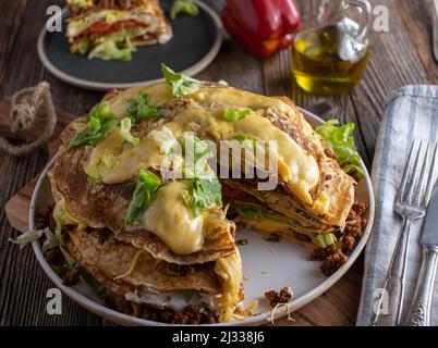 Pikanter Pfannkuchenstapel im Tex-Mex-Stil mit Hackfleisch, Bohnen, Tomaten, Sauerrahm, Salat und Käse Stockfoto