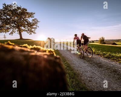 Zwei Schotterbiker fahren auf Veiglberg bei Wolfsratshausen in den Sonnenuntergang Stockfoto