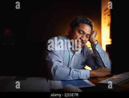 Die langen Stunden haben ihn erschöpft. Aufnahme eines reifen Geschäftsmannes, der an seinem Schreibtisch schläft, während er spät in einem Büro arbeitet. Stockfoto