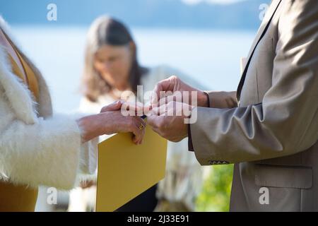 Ältere Braut und Bräutigam während ihrer Hochzeitszeremonie, während der Bräutigam Ring auf den Finger der Braut legt. Wir heiraten wieder. Wir haben wieder geheiratet. Stockfoto