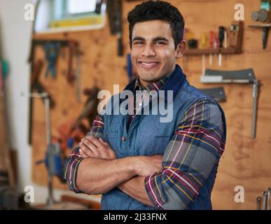 Sie nennen es, und ich kann es bauen. Porträt eines glücklichen Handwerkers, der mit gefalteten Armen in seiner Werkstatt steht. Stockfoto