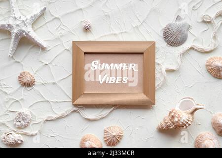 Text Sommer Vibes in goldenem Rahmen. Weißer Hintergrund mit Seesternen, Muscheln, Muscheln, Muscheln, Halskette. Fischernetz auf cremebeige braun einfarbig Stockfoto