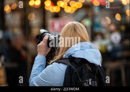 Blonde Frau mittleren Alters mit einer Fotokamera am Abend auf den Straßen der Stadt, Lifestyle-Konzept Stockfoto