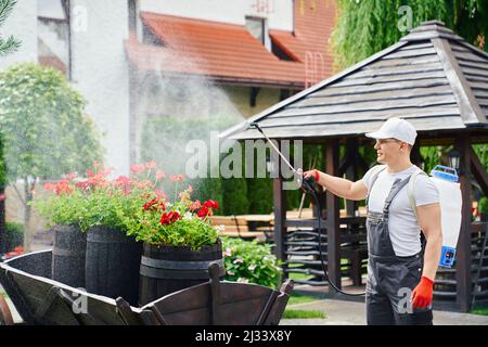 Professioneller männlicher Gärtner in Uniform, Schutzbrille und Handschuhe mit Aerosol-Chemikalienschutz vor Schädlingen während der Arbeit im Garten. Konzept von Menschen, Pflanzen und Saisonarbeit. Stockfoto