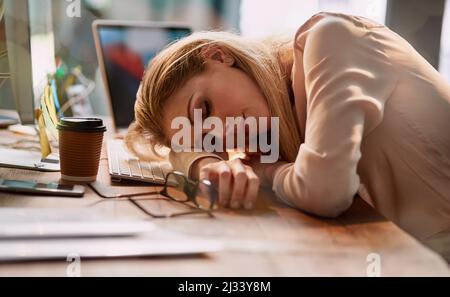 Lange Stunden fordern ihren Tribut. Aufnahme einer erschöpften jungen Geschäftsfrau, die an ihrem Schreibtisch in einem Büro schläft. Stockfoto