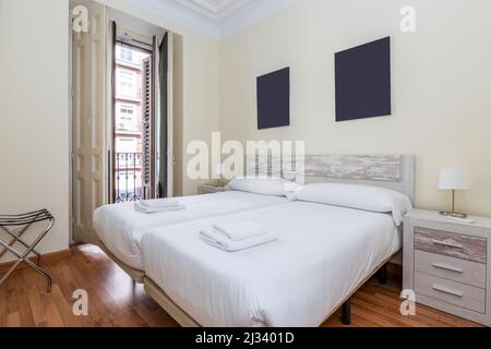 Schlafzimmer mit zwei Betten mit weißer Bettwäsche, Kopfteil aus Holz und weiß lackierter Zimmerei, Balkon mit Holzfensterläden, passendem Nachttisch Stockfoto