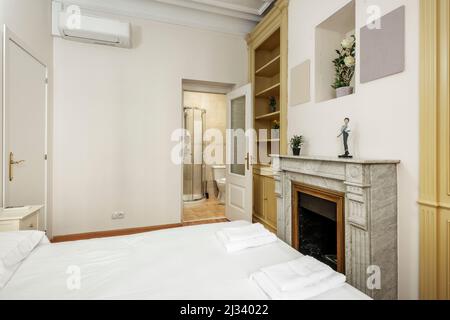 Schlafzimmer mit Doppelbett, Klimaanlage, weißem Marmorkamin, Holzregalen und Duschkabine im eigenen Bad Stockfoto