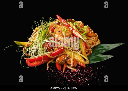 Udon-Nudeln mit Meeresfrüchten, gemischtes Gemüse, Garnelen, Muscheln, Tintenfisch, tonkatsu-Sauce, Chili, grüne Zwiebel, Lauch. Isoliert auf schwarzem Backgrou Stockfoto