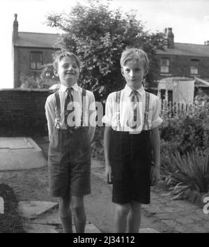 1960s, historisch, zwei junge Jungen, Brüder, die draußen in einem Garten für ihr Foto stehen, mit Hemd und Krawatten und kurzen Hosen, von Hosenträger hochgehalten, Stockport, Manchester, England, Großbritannien. Stockfoto