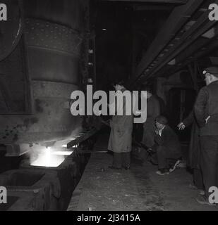 1950s, historischer Stahlarbeiter und Betriebsleiter neben einem Hochofen, der die Produktion von geschmolzener Eisenflüssigkeit in der Fabrik der Steel Company of Wales, Abbey Works, Port Talbot, Wales, Großbritannien, überwacht. Stockfoto