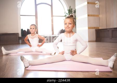 Zwei schöne Mädchen, die während des Tanzchoreografen-Kurses Beine streckend auf dem Boden sitzend machen Stockfoto