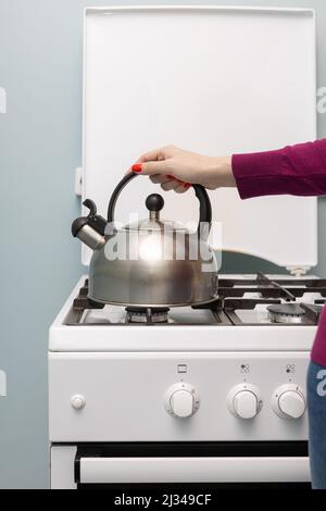 Weibliche Hand legt einen Metallkessel auf einen Gasbrenner Stockfoto