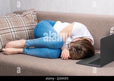 Junge Frau, die in der Nähe des Laptops verärgert liegt. Das Konzept des Burnout am Arbeitsplatz, des Scheiterns im Home Office. Stockfoto