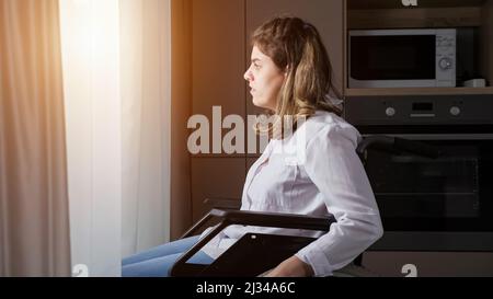 Behinderte Frau bewegt sich im Rollstuhl näher an das Fenster zu Hause Stockfoto