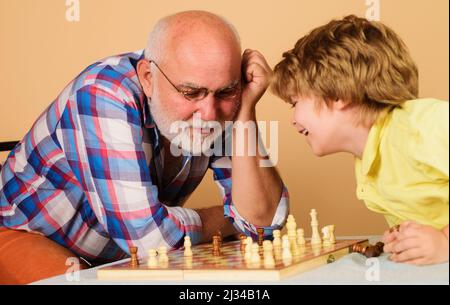 Großvater lehrt Enkel Schach zu spielen. Älterer Mann, der über den nächsten Schachzug nachdenkt. Stockfoto