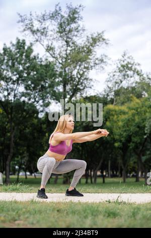 Fit junge Frau tut Kniebeugen im Freien Stockfoto