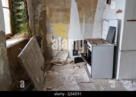 Alte verlassene und schmutzige Küchenausstattung in einer leeren Wohnung. Verwitterte Innenelemente in einer Ruine. Ein Herd und eine Holztür liegen herum. Stockfoto