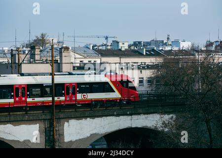 Warschau. Polen. 03.30.2022. Ein moderner Zug fährt über die Brücke auf dem Hintergrund von Stadtgebäuden. Stockfoto