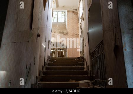 Dunkle Treppe in einem verlassenen Gebäude. Die Tapete blättert von den Wänden ab. Schmutzige Stufen nach oben zum nächsten Stock. Innenausstattung in schlechtem Zustand. Stockfoto