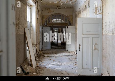 Langer Korridor in einem verlassenen öffentlichen Gebäude mit vielen Holztüren. Urbane Erkundung in einem großen alten Haus. Die Farbe blättert von den Wänden. Stockfoto