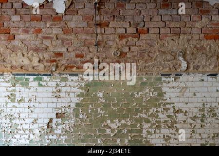 Verwitterte alte Steinmauer mit roten Ziegeln und grünen Fliesen. Die Farbe blättert vom Gebäude ab. Hintergrundtextur einer schmutzigen realen Oberfläche. Beschädigte Ruine Stockfoto