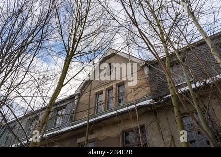 Verlassene Gebäude mit einer beschädigten Fassade und kaputten Fenstern. Blick auf ein leeres Haus mit dem blauen Himmel im Hintergrund. Verlorener Ort Stockfoto