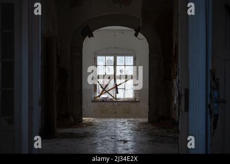 Kaputtes Fenster am Ende des Korridors in einem alten dunklen Gebäude. Verlassene Haus in einem beschädigten Zustand. Gruselige Innenausstattung in einer schmutzigen und veralteten Ruine. Stockfoto