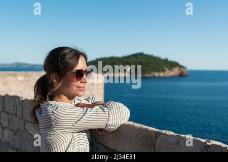 Die Frau blickt von den Stadtmauern der Altstadt in Dubrovnik, Dalmatien, Kroatien auf das Meer. Stockfoto