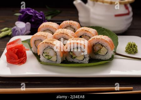 Maki Sushi Kimono mit Dekor. Mit Lachs, Garnelen, Gurke, auf einem Teller, auf einem Holzhintergrund Stockfoto