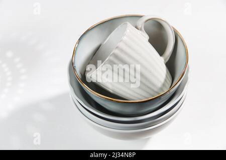 Eine Pyramide aus weißen Schalen, Tellern und Tassen in verschiedenen Größen und Farben auf einem beigen Tisch in der Küche. Skandinavischer Stil. Ort für Ihren Text. Kopieren Stockfoto