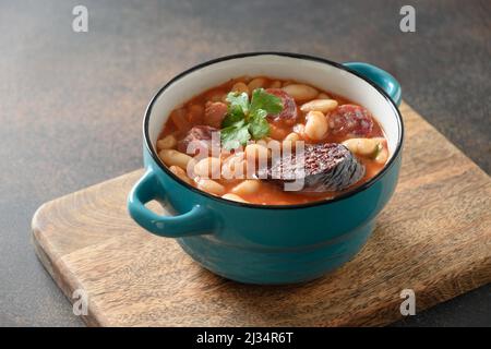 Asturiana traditionelle Eintopf Fabada mit Harikot, Tomaten, Blutwurst auf braunem Hintergrund. Nahaufnahme. Stockfoto