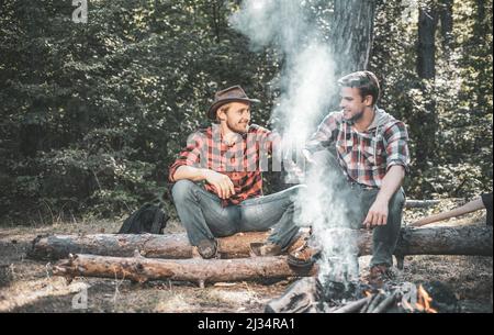 Zwei gutaussehende Männer Freunde auf Camping in der Nähe Lagerfeuer. Freunde Männer Wanderer beobachten gemeinsam Feuer im Lager. Zwei Freunde verbringen ihr Wochenende mit einem Picknick Stockfoto