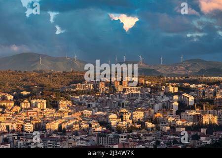 Windturbinen auf den Hügeln in Kusadasi Türkei mit einer Stadtlandschaft vor und dramatischen Wolken im Hintergrund. Stockfoto