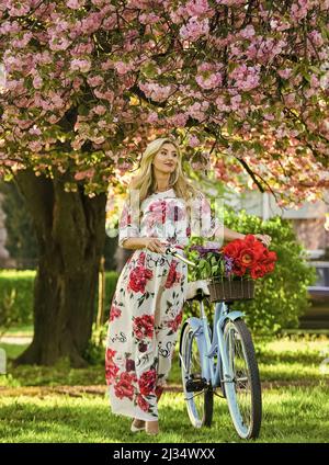 Sakura-Saison. Tourismuskonzept. Transport und Reisen. Mädchen langes Kleid Retro Cruiser Fahrrad Sakura Baum. Frühlingsferien. Frau mit Tulpen Stockfoto