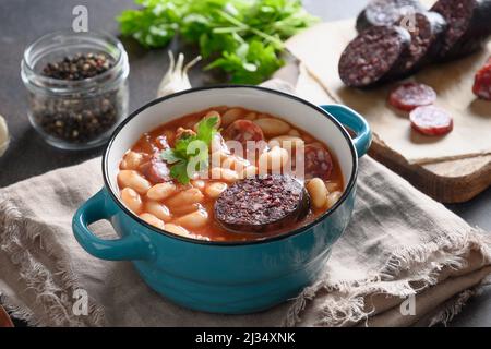 Asturiana traditionelle Eintopf Fabada mit Harikot, Tomaten, Blutwurst auf braunem Tisch. Nahaufnahme. Stockfoto