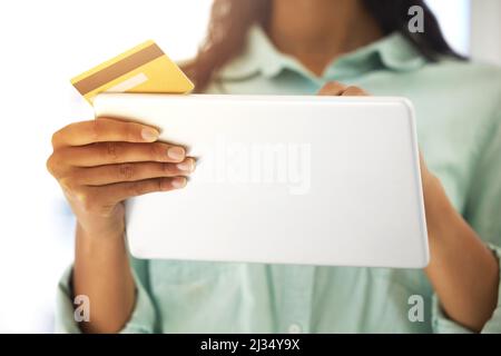 Müssen einige schnelle Zahlungen zu machen. Ausgeschnittene Aufnahme einer nicht erkennbaren Person, die eine Kreditkarte und ein digitales Tablet verwendet, um zu Hause online einzukaufen. Stockfoto