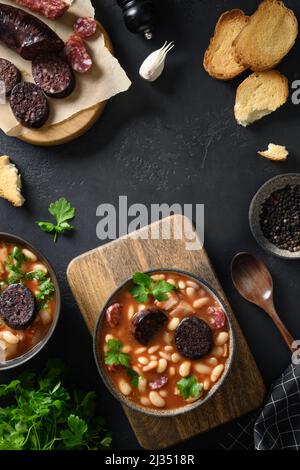 Zwei Portionen Asturiana spanish Fabada mit Chorizo, Morcilla, Wurst, Haricot serviert frischen Toast auf schwarzem Hintergrund. Draufsicht. Vertikales Format. Kopieren Stockfoto