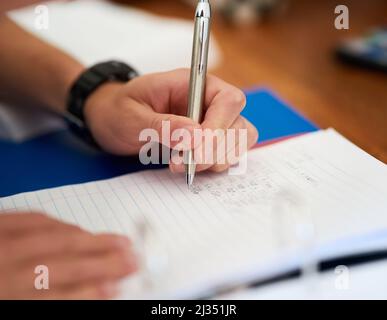 Hes fleißig über seine Hausaufgaben. Nahaufnahme eines nicht identifizierbaren Mannes, der seine Hausaufgaben zu Hause macht. Stockfoto