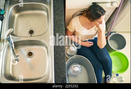 Besorgt über das Wasser. Eine schöne junge Frau, die sich über die Wasserkrise deprimiert fühlt, während sie auf dem Boden sitzt Stockfoto