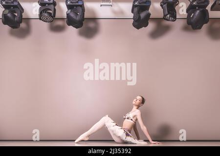 Junge schöne anmutige kaukasische Ballerina Praxis Ballett Positionen in Tutu Rock. Klassische Balletttänzerin, die im Studio auf dem Boden sitzt Stockfoto