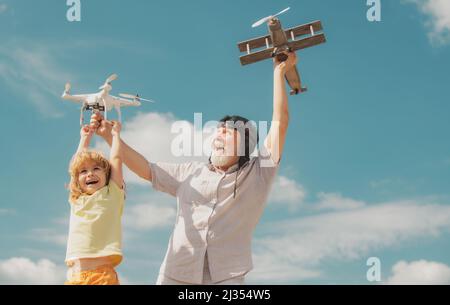 Enkelkind und Großvater spielen mit Spielzeugflugzeug und Quadcopter-Drohne gegen den Himmel. Kind Pilot Flieger mit Flugzeug träumt von Reisen. Familie Stockfoto
