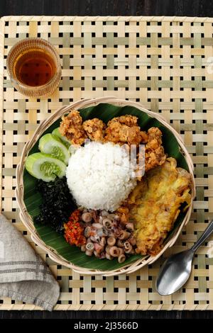 Draufsicht Nasi Campur Cumi-Ase, Weißer Reis mit sautiertem gesalzenem Tintenfisch, Sambal, Ei, Kulit Ayam knusprige Hühnerhaut und gekochtes Cassava-Blatt. Stockfoto