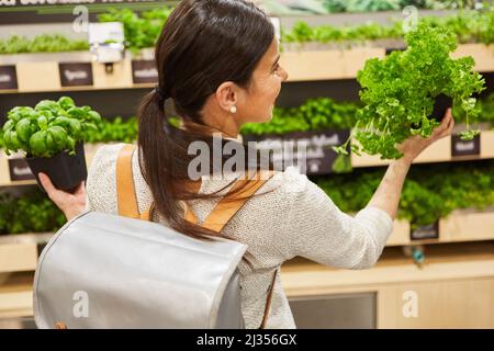 Junge Frau als Kundin beim Einkauf frischer Kräuter am Gemüsestand im Supermarkt Stockfoto