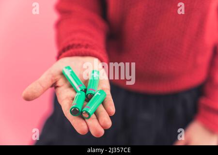 Zwei Handflächen einer kaukasischen Person mit vier Batterien auf rosa Hintergrund. Ökologie und Recycling-Konzept. Hochwertige Fotos Stockfoto