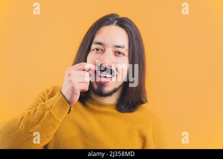 Movember in Aktion. Fröhlicher langhaariger kaukasischer Mann mit gelbem Sweatshirt und gefälschtem Schnurrbart. . Hochwertige Fotos Stockfoto