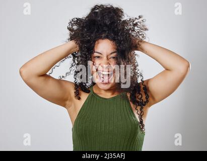Der natürliche Haarkampf ist real. Studioaufnahme einer Frau mit unordentlichen Haaren, die vor einem grauen Hintergrund posiert. Stockfoto